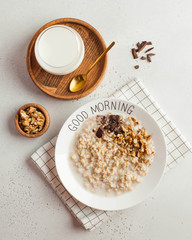 Oatmeal porridge on a plate that says good morning with chocolate and nuts and a cup of milk. Healthy food. Breakfast.
