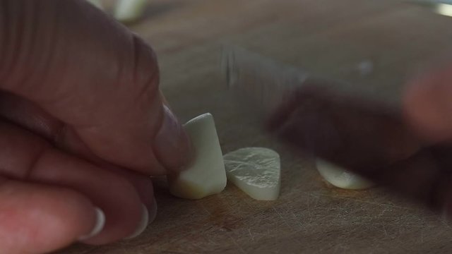 A clove of garlic is cut by a cook on a wooden cutting Board.