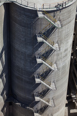 Grey concrete tower with pipes and stair.  Close-up of cement plant silo. © Alexey Rezvykh