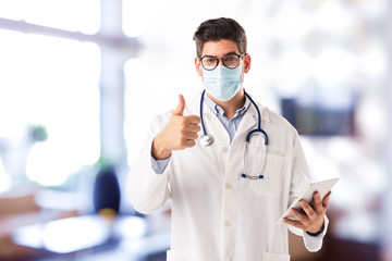 Male doctor wearing face mask and giving thumbs up while standing in the hospital