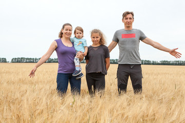 Husband and wife with their preteen age daughter and toddler child, mother holding baby on arms, four Caucasian people family standing on golden wheat field