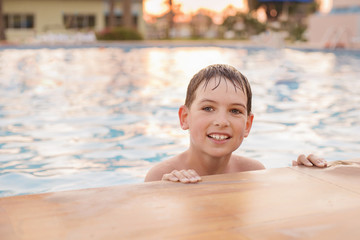 a boy of European appearance 7 years old swims in the pool at sunset