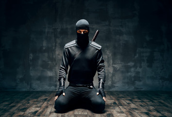 Ninja kneeling posing with a sword over black background - obrazy, fototapety, plakaty