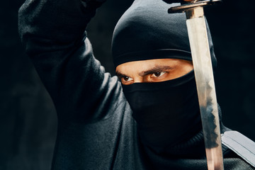 Fighting ninja posing with a sword over black background