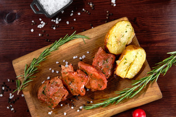 Grilled pork kebab with potatoes, on a wooden plate, decorated with herbs and tomato sauce. Top view.
