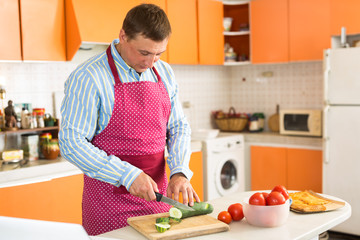 Portrait of adult man in apron cutting fresh vegetables, preparing vegetarian dinner at home kitchen