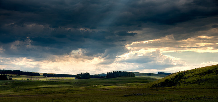 panorama of the Aubrac plateau in the evening with dramatic storm clouds & sun rays, rustic rural scene, Lozere France