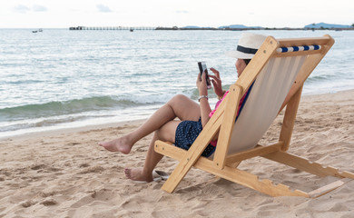 Young woman using a mobile phone on the beach chair on vacation.