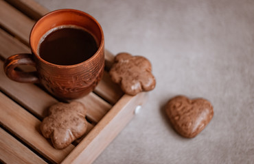 Ceramic mug with coffee on a wooden tray, near chocolate chip cookies in the shape of flowers and a heart