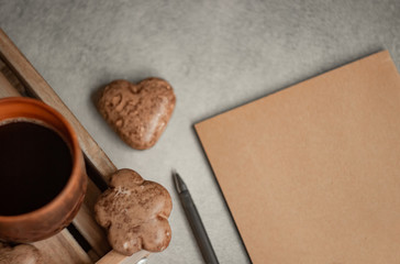 Brown coffee mug and chocolate chip cookies on a wooden tray, heart-shaped cookies and notebook and pencil