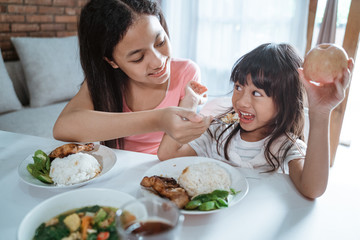 little girl is excited when her older sister feed her while eating together at the dining table against the dining room background
