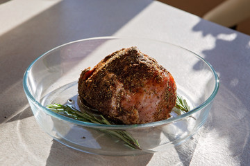 A piece of meat with rosemary in a glass dish