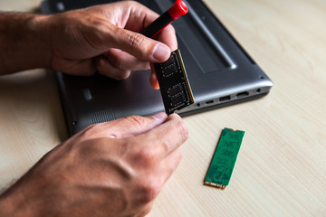 A human hand with a computer memory frame. He wants to install it in the laptop computer on the desk.
