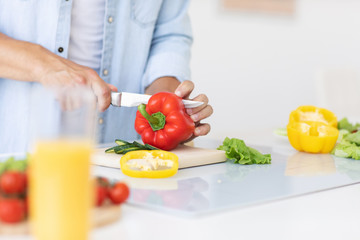 Man cuts red peppers for salad at home kitchen close-up.