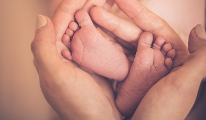 Obraz na płótnie Canvas Baby feet in mother hands. Tiny Newborn Baby's feet on female Heart Shaped hands closeup. Mom and her Child. Happy Family concept. Beautiful conceptual image of Maternity.