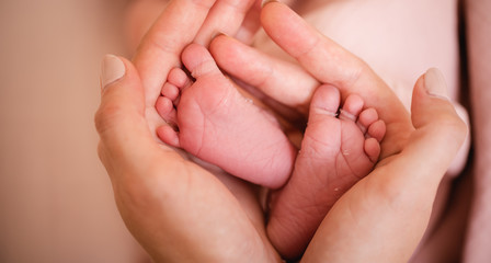Baby feet in mother hands. Tiny Newborn Baby's feet on female Heart Shaped hands closeup. Mom and her Child. Happy Family concept. Beautiful conceptual image of Maternity.