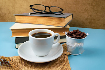 Cup of coffee and stack of books on blue background