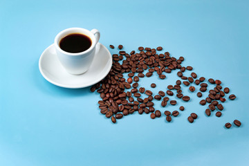 Cup of coffee and scattered coffee beans on blue background