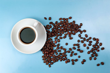 Cup of coffee and scattered coffee beans on blue background
