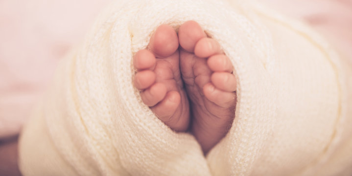 Tiny foot of newborn baby. Soft newborn baby feet against a pink blanket. Baby girl feet with toes curled up.