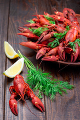 Red crayfishes on plate served with dill and lemon, dark wooden background, vertical