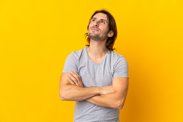 Young handsome man isolated on yellow background looking up while smiling