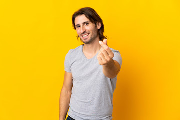 Young handsome man isolated on yellow background making money gesture