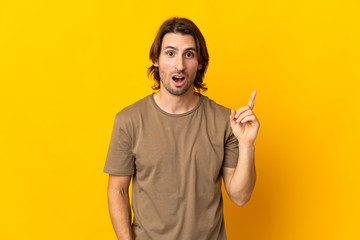 Young handsome man isolated on yellow background intending to realizes the solution while lifting a finger up