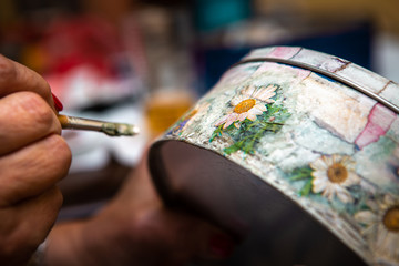 Close-up of a flower motif on a box on which a woman makes a decoupage.