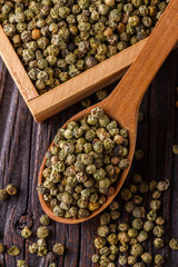 green peppercorns in wooden scoop on rustic background