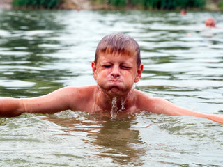 Water runs down the face of a Caucasian boy emerging from the lake
