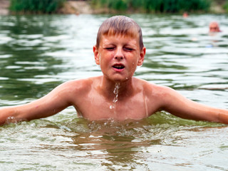 Water runs down the face of a Caucasian boy emerging from the lake