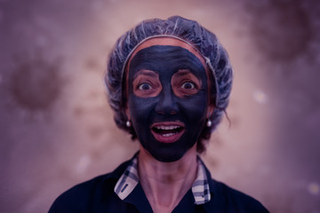 Brazilian woman with happy expression and gray clay mask. Concept: beauty, face care, facelift, wellness, skin care. Shot with covid background