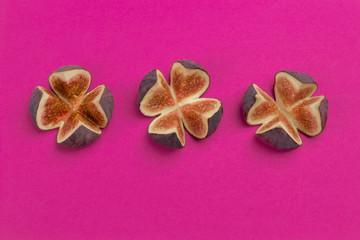 The three figs are cut into four slices. Bright pink background.