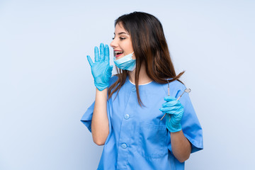 Woman dentist holding tools over isolated blue background shouting with mouth wide open