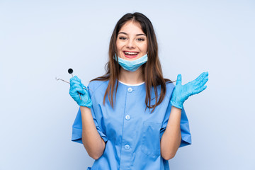 Woman dentist holding tools over isolated blue background unhappy and frustrated with something