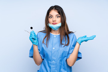 Woman dentist holding tools over isolated blue background having doubts with confuse face expression
