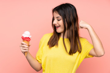 Young brunette woman holding a cornet ice cream over isolated pink background celebrating a victory