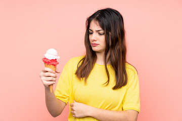 Young brunette woman holding a cornet ice cream over isolated pink background with sad expression