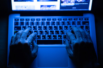 Soft focus hands of a man using laptop computer for hacking or steal data information at night in office. Hacking data concept.