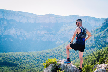 Naklejka premium Runner man up on a mound of rocks looking at the mountains.