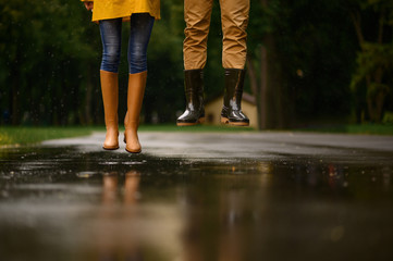 Love couple jumps in a puddle in park, rainy day