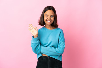 Young latin woman isolated on pink background saluting with hand with happy expression