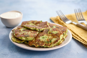 Vegetarian zucchini fritters or pancakes, served with greek yogurt on blue background, horizontal.