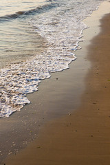 Small waves and ripples on a golden sandy beach. Early morning sunlight