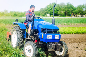 Obraz premium A farmer drives a tractor while working on a farm field. Loosening surface, cultivating the land. Farming, agriculture. Use of agricultural machinery and equipment to simplify and speed up work.