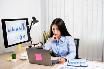 Asian woman working on a laptop with a cheerful and happy smile while working at the office