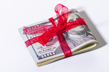 Banknotes of 100 American dollars are folded in half and tied with a red ribbon close-up on a light background.