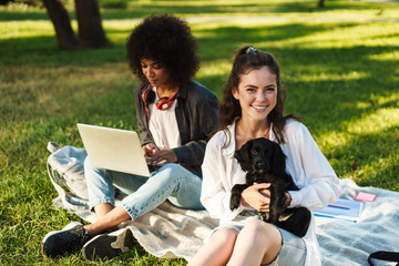 Image of multinational women using laptop while sitting with puppy
