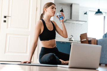 Fototapeta na wymiar Attractive tired young fitness woman drinking water